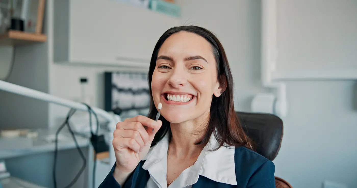 Smiling patient holding a shade guide at the dental chair